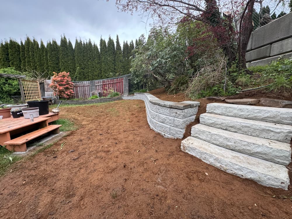 Landscaped garden with stone steps and retaining wall, surrounded by trees and shrubs.