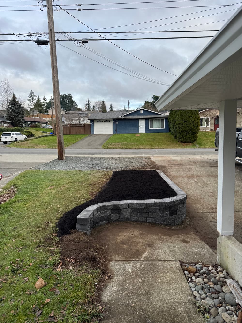 Newly landscaped yard featuring a stone retaining wall filled with dark mulch.