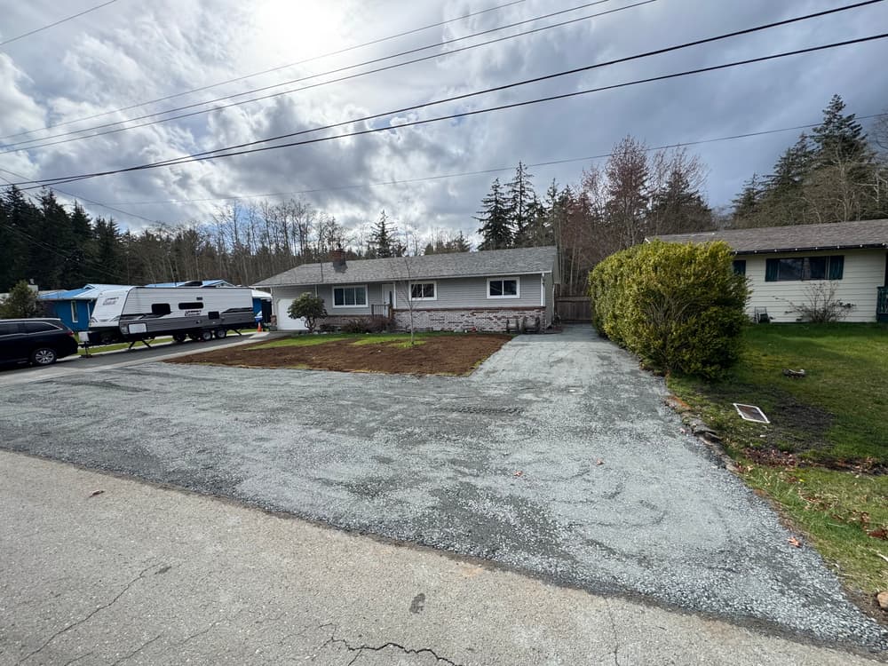 Residential area featuring a freshly cleared lot, house, and trees under a cloudy sky.