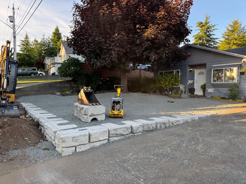 Residential landscaping project featuring gravel driveway with retaining wall and construction equipment.