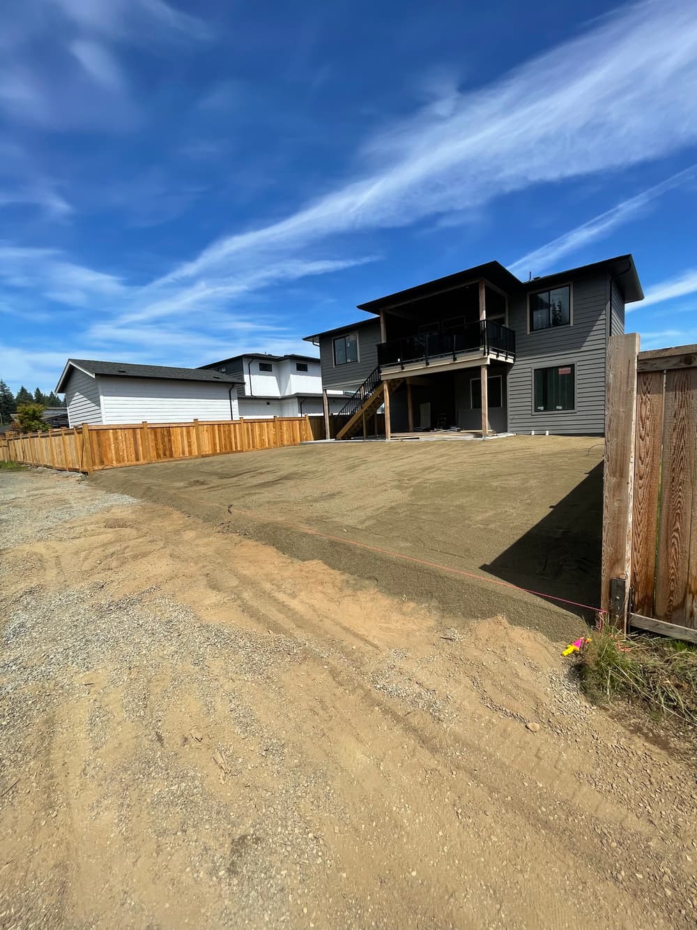 Newly constructed house with a spacious yard and gravel driveway under a clear blue sky.
