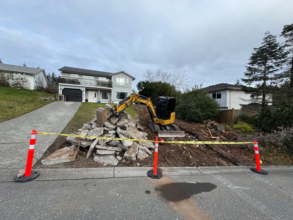 Excavator clearing rubble at residential construction site with safety barriers.