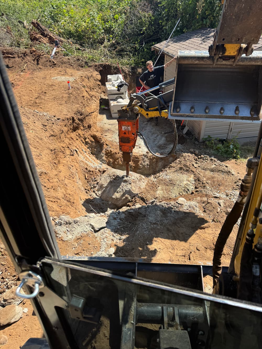 Excavation site with worker using jackhammer near machinery and dirt piles.