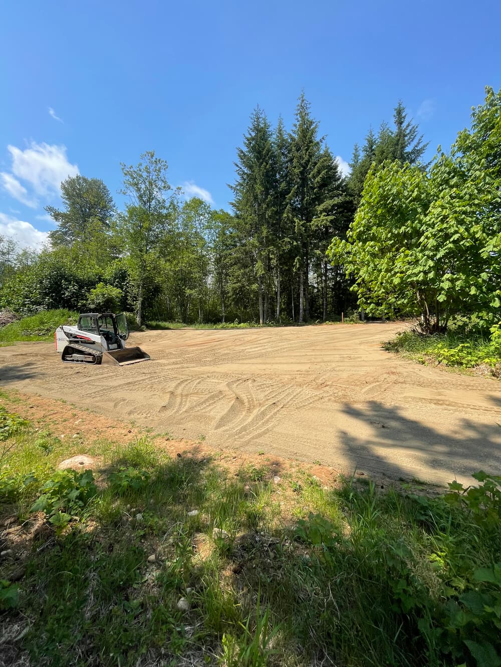 Cleared land with a skid steer, surrounded by trees and blue sky, prepared for construction.