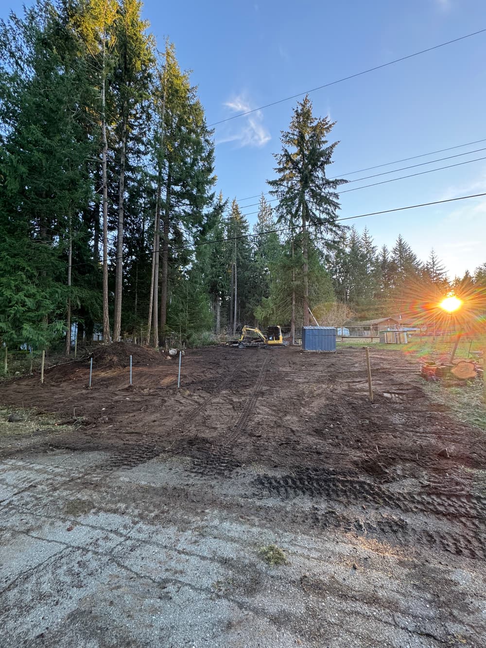 cleared land for construction with trees, machinery, and a sunset in the background