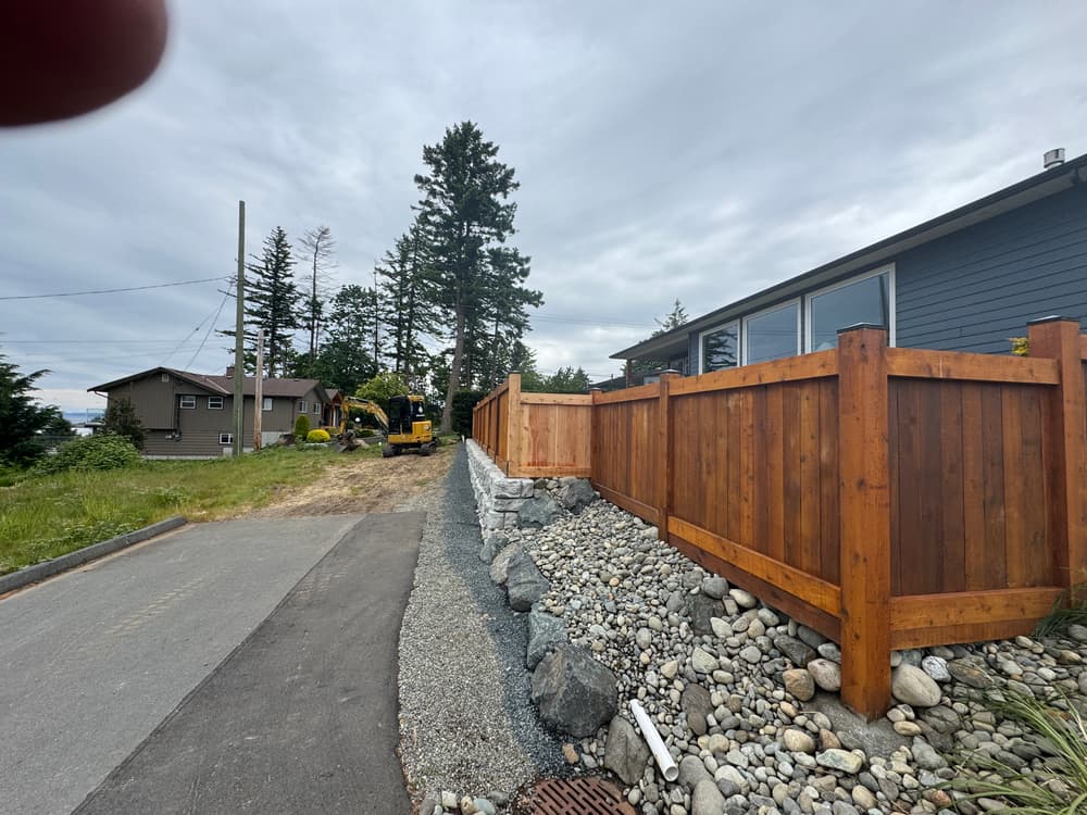Residential property with wooden fence, gravel pathway, and construction equipment in background.