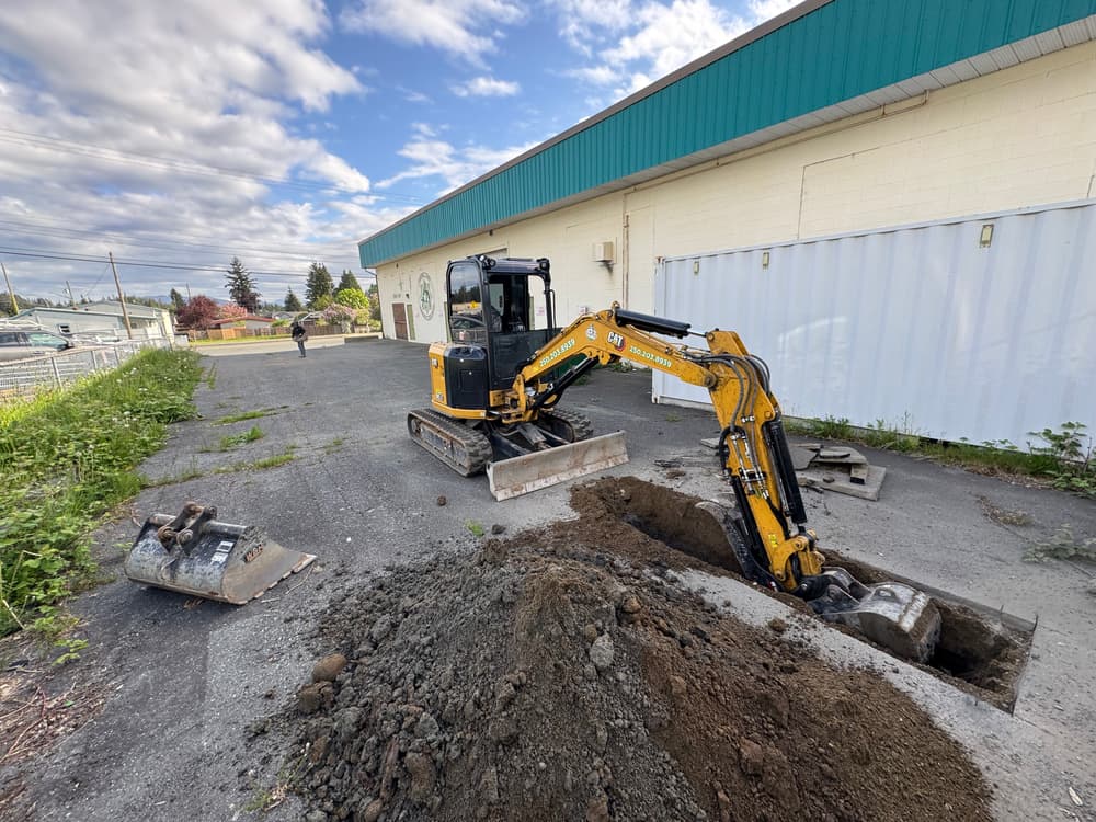 Excavator digging a trench on a construction site with cloudy skies in the background.