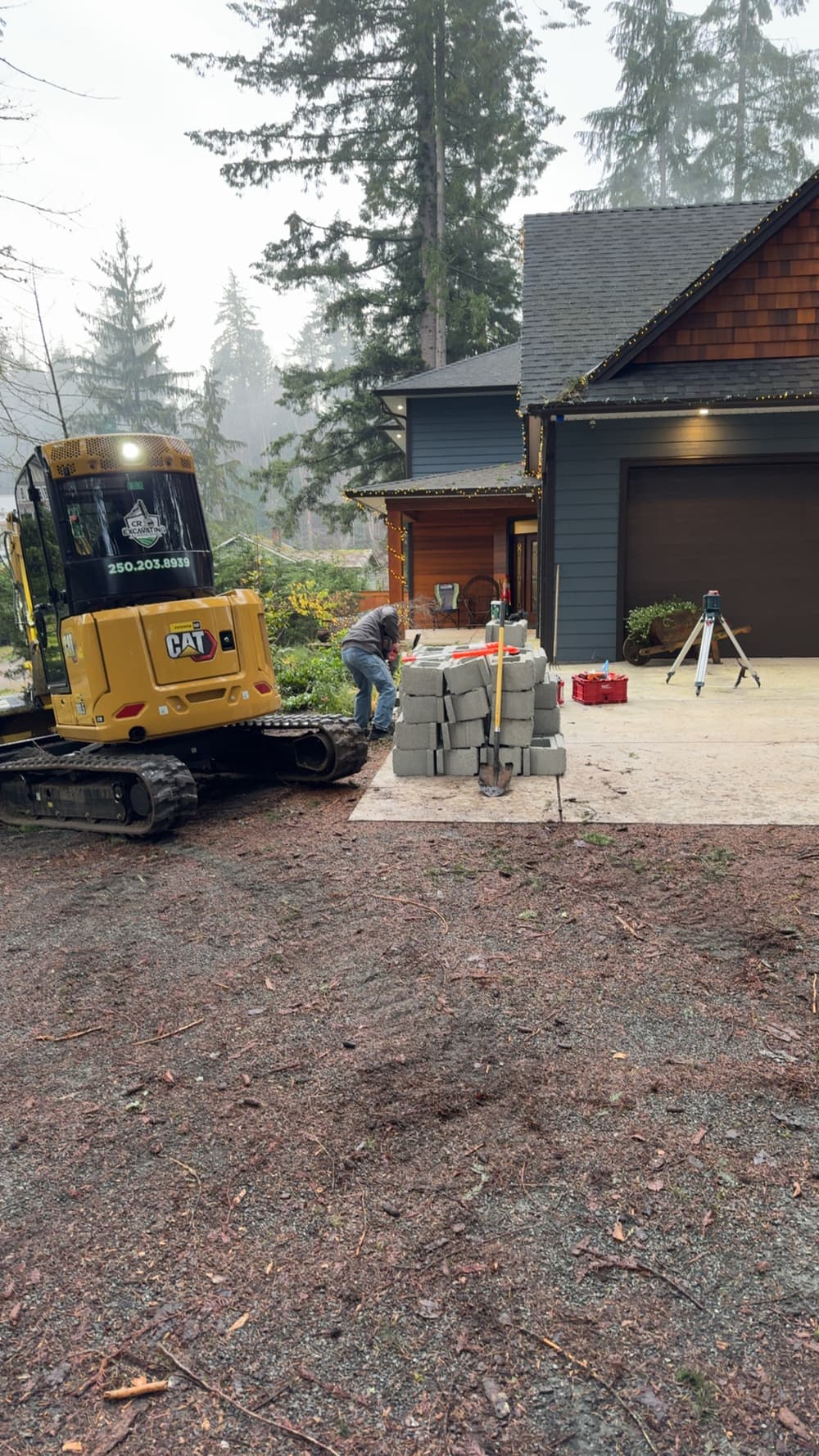 Construction worker using a mini excavator to place concrete blocks near a home.