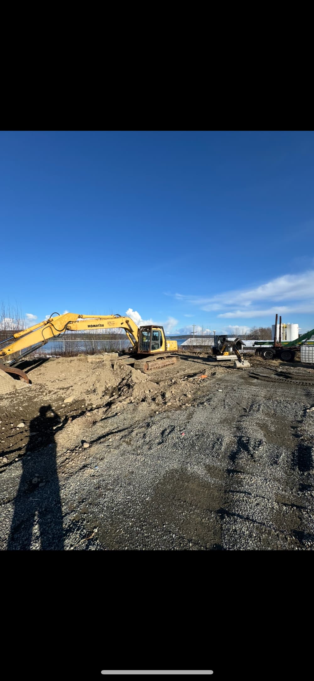 Excavators at a construction site with clear blue sky and gravel ground.