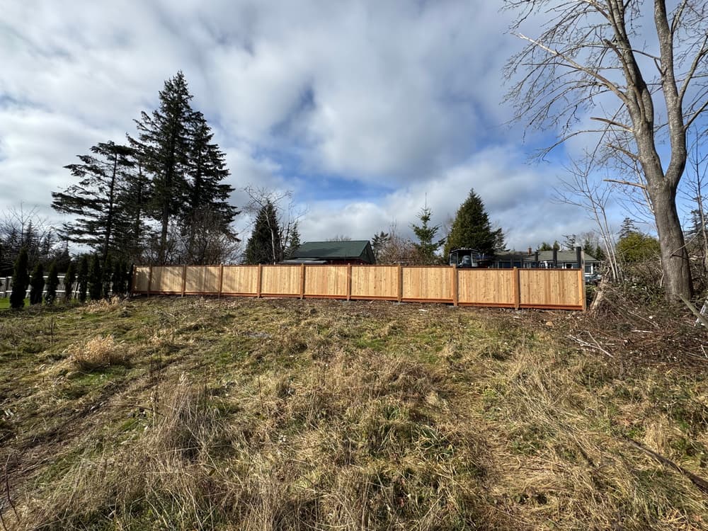 Wooden fence dividing property with trees and cloudy sky in the background, showcasing landscape.