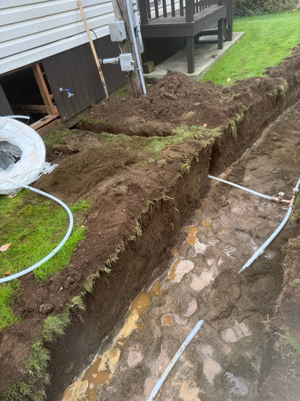 Trenched yard with exposed pipes and muddy ground for home plumbing installation.