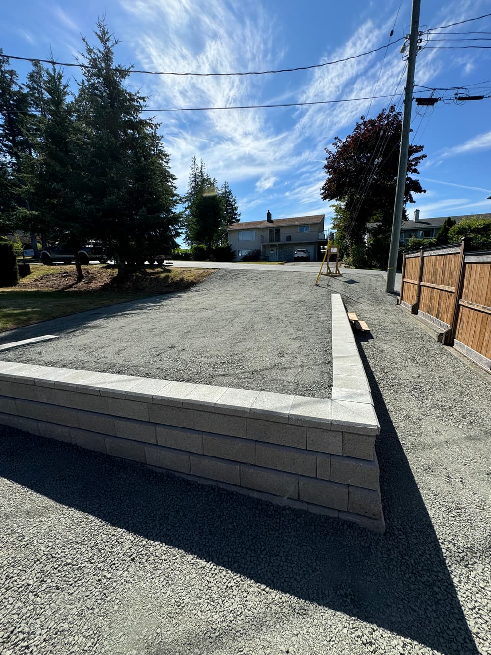 Gravel driveway with concrete border under a blue sky and trees in a residential area.