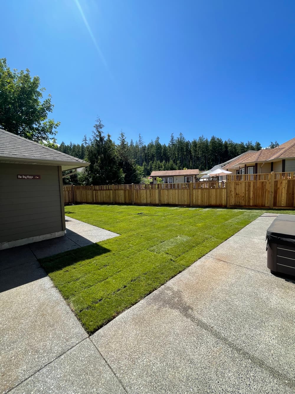 Spacious backyard with green lawn and wooden fence under clear blue sky.