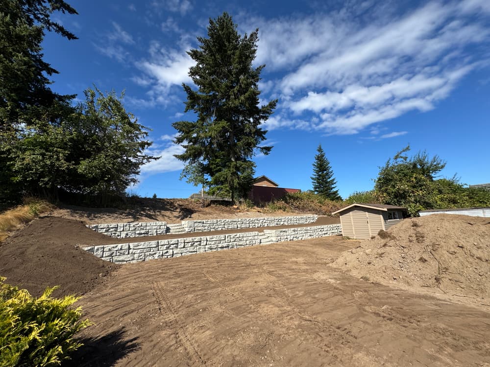 Landscape with multi-level stone retaining walls, dirt path, and trees under a blue sky.