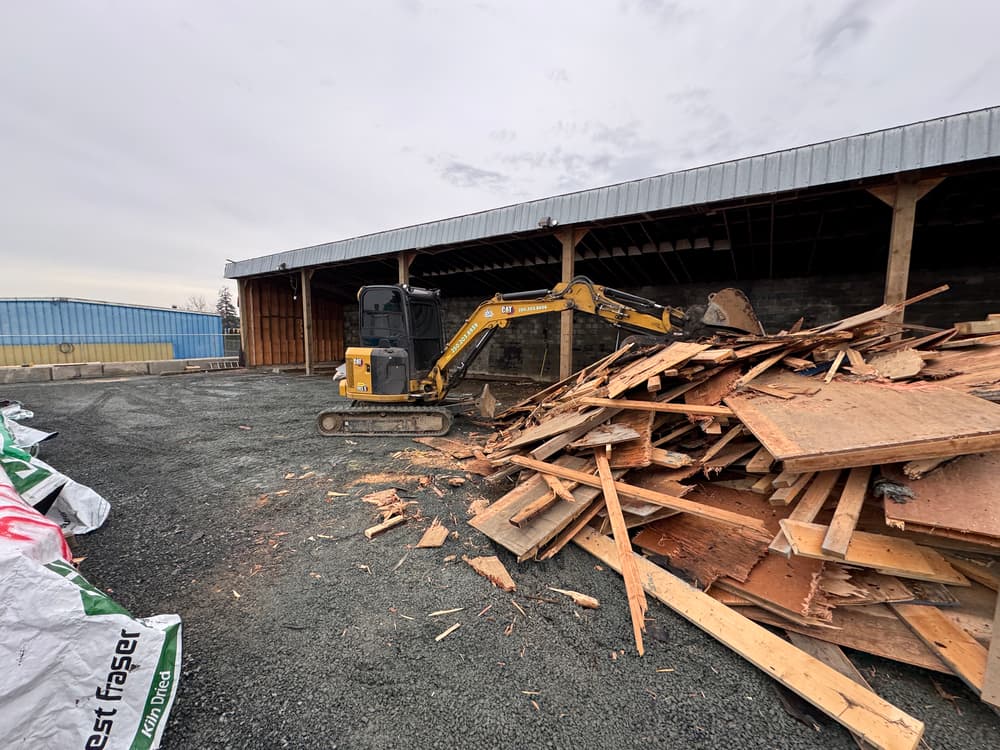 Excavator on construction site near debris pile and building structure.