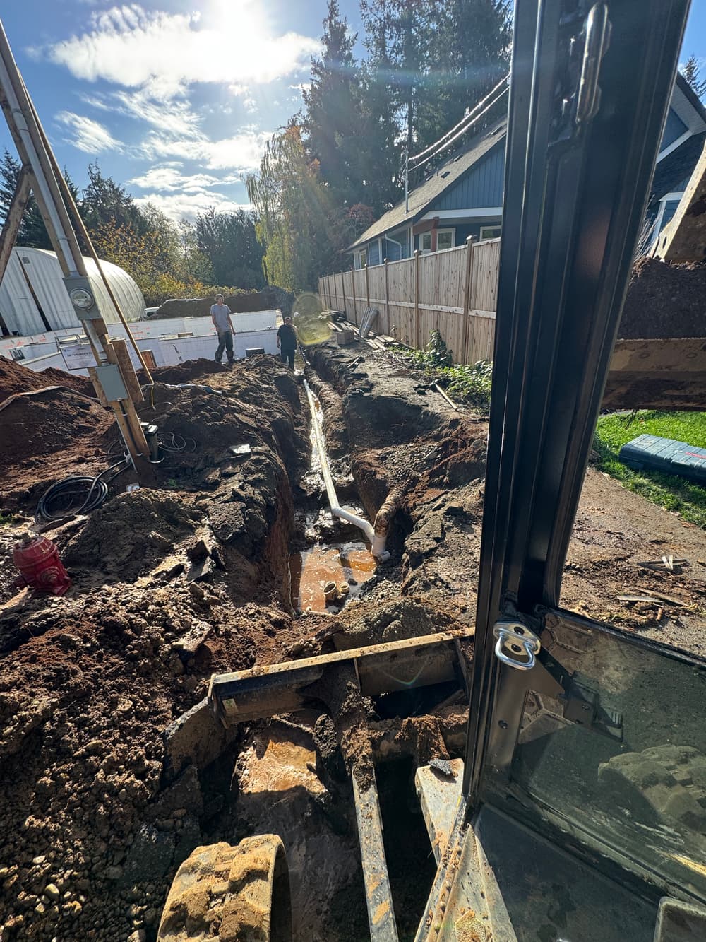 Excavation site with workers digging trench for utility installation under sunny sky.